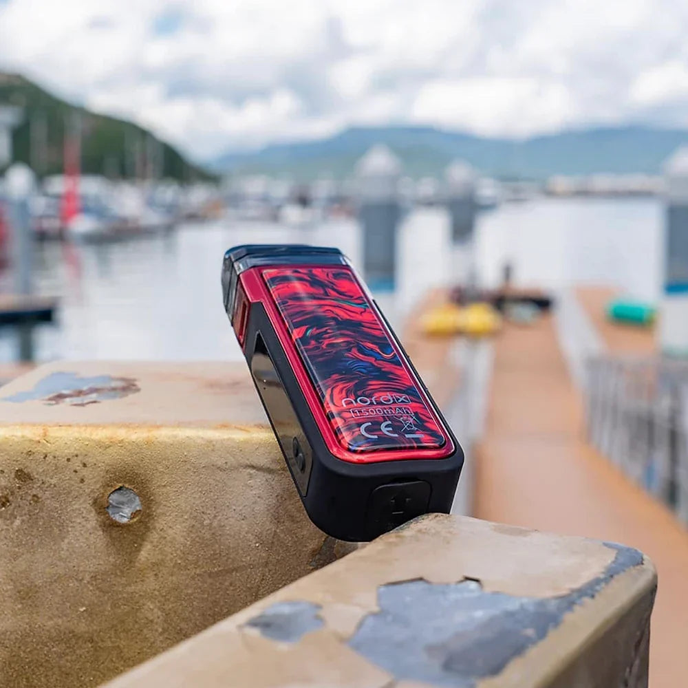 Red SMOK NORD X Pod System with 60W power and IP67 rating, placed on dockside railing, ideal for outdoor vape use.