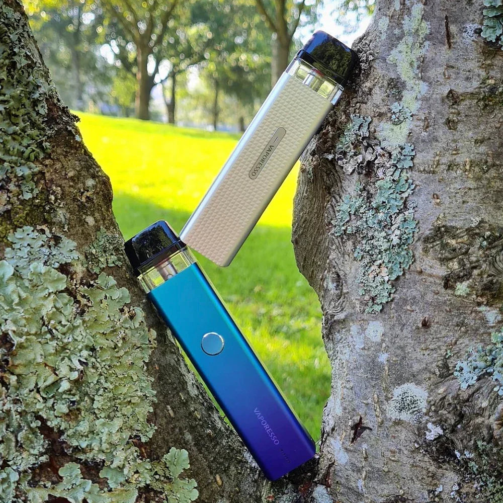 Two Vaporesso XROS 2 Pod Systems in silver and gradient blue resting on tree bark, showing off stylish color variants and portability.