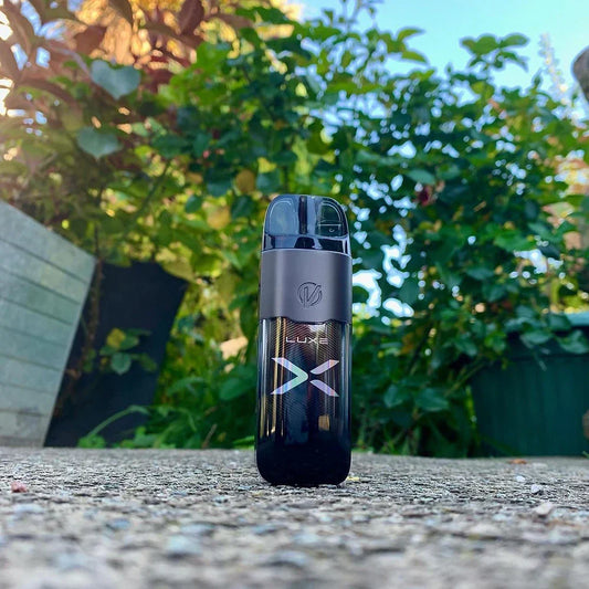 Vaporesso LUXE X 40W Pod System with 5mL pod and 1500mAh battery standing upright outdoors on concrete, surrounded by greenery.