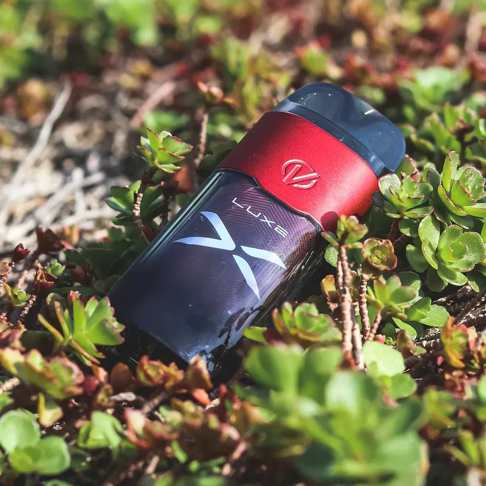 Red Vaporesso LUXE X 40W Pod System with integrated coil and zinc-alloy body lying on green ground cover plants.