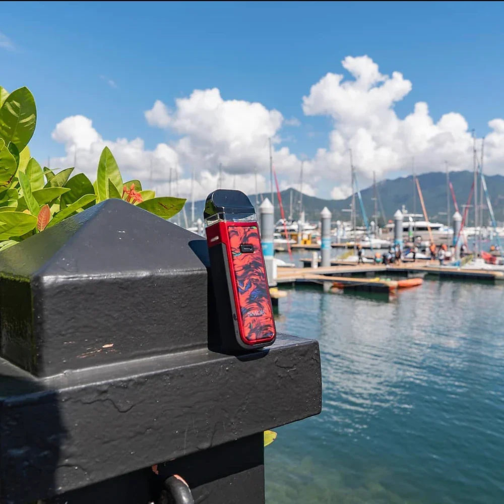Red SMOK NORD X Pod System displayed at marina, emphasizing portable design and IP67 protection for vape enthusiasts.