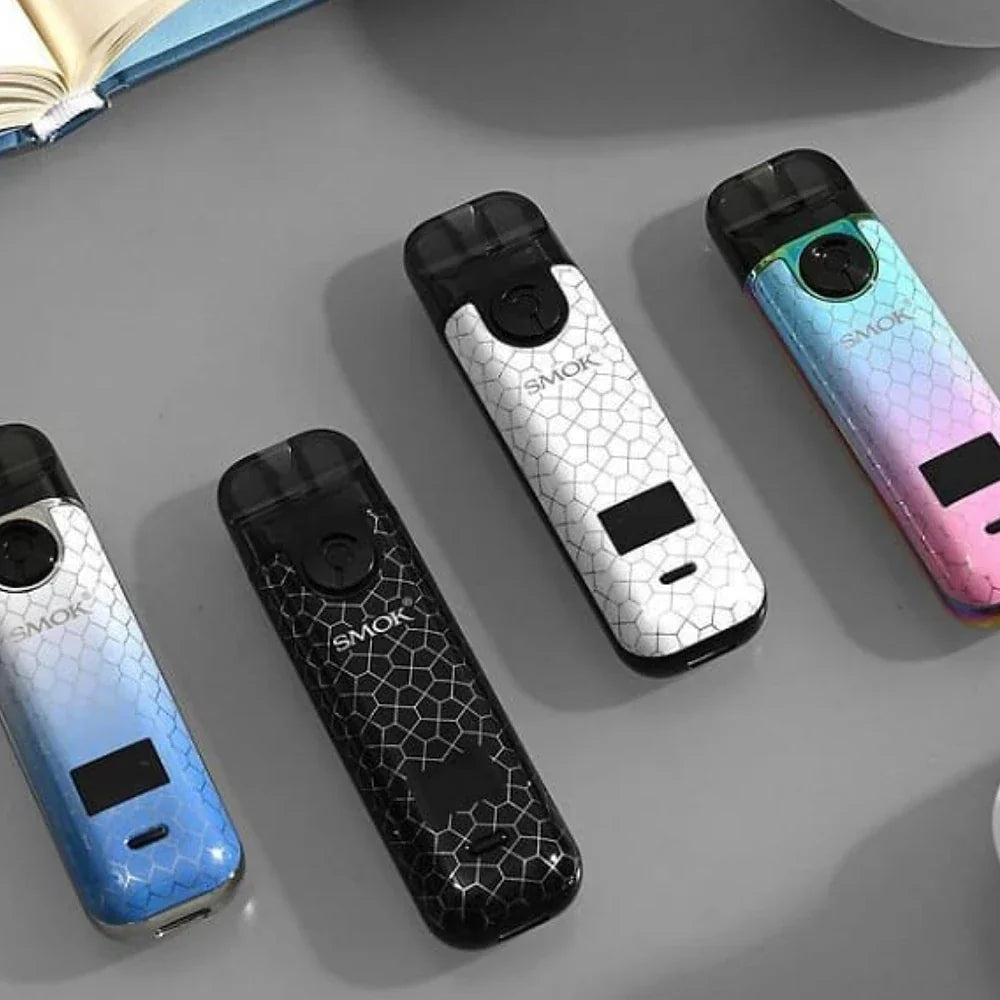 Four SMOK NOVO 4 Pod Kits - 25W in black, white, blue, and pink gradient colors arranged on a gray surface, showing color variety and OLED display.