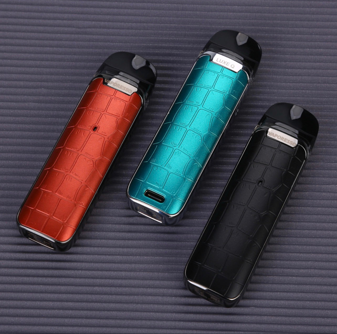 Three Vaporesso Luxe Q Pod Systems in red, teal, and black on textured surface, highlighting stylish design and portable vape performance.