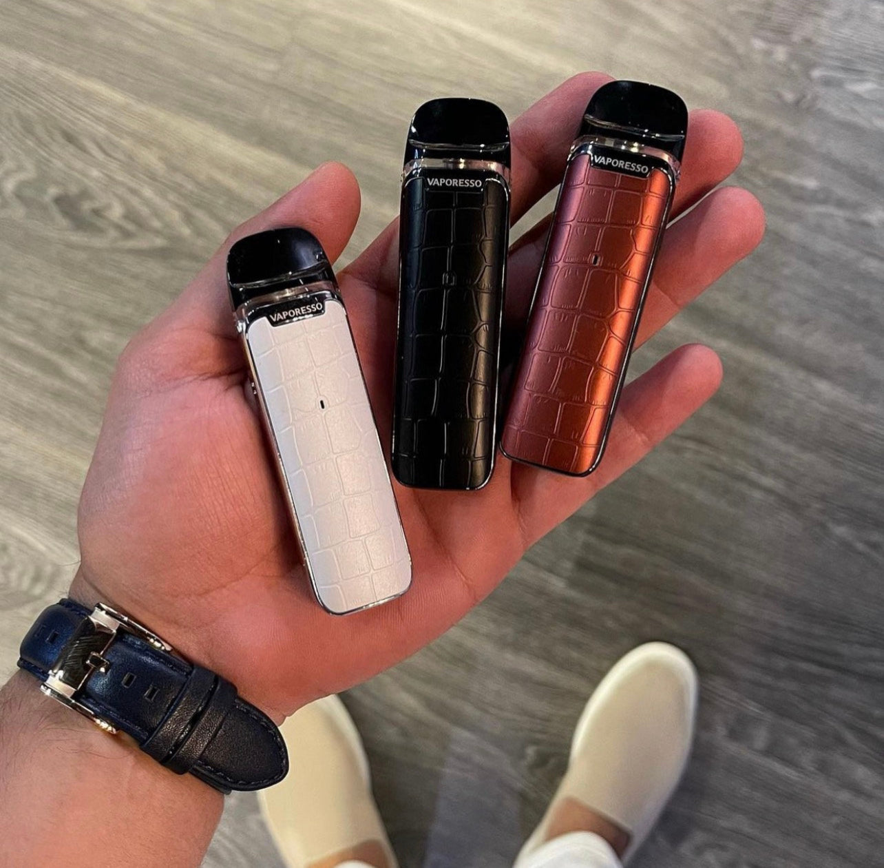 Hand holding three Vaporesso Luxe Q Pod Systems in white, black, and red, highlighting compact size and textured anti-slip finish.